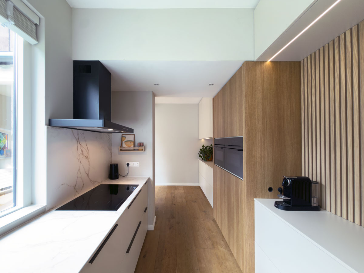 Ontwerp van een keuken op maat met beige deurtjes en houten latjes met ledstrips en een marmeren aanrechtblad.