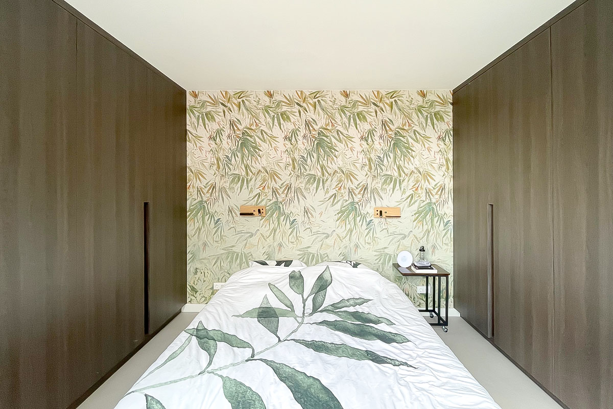 Luxe inbouwkasten en kasten op maat slaapkamer in donkere houtprint met een groen behang met bladeren.