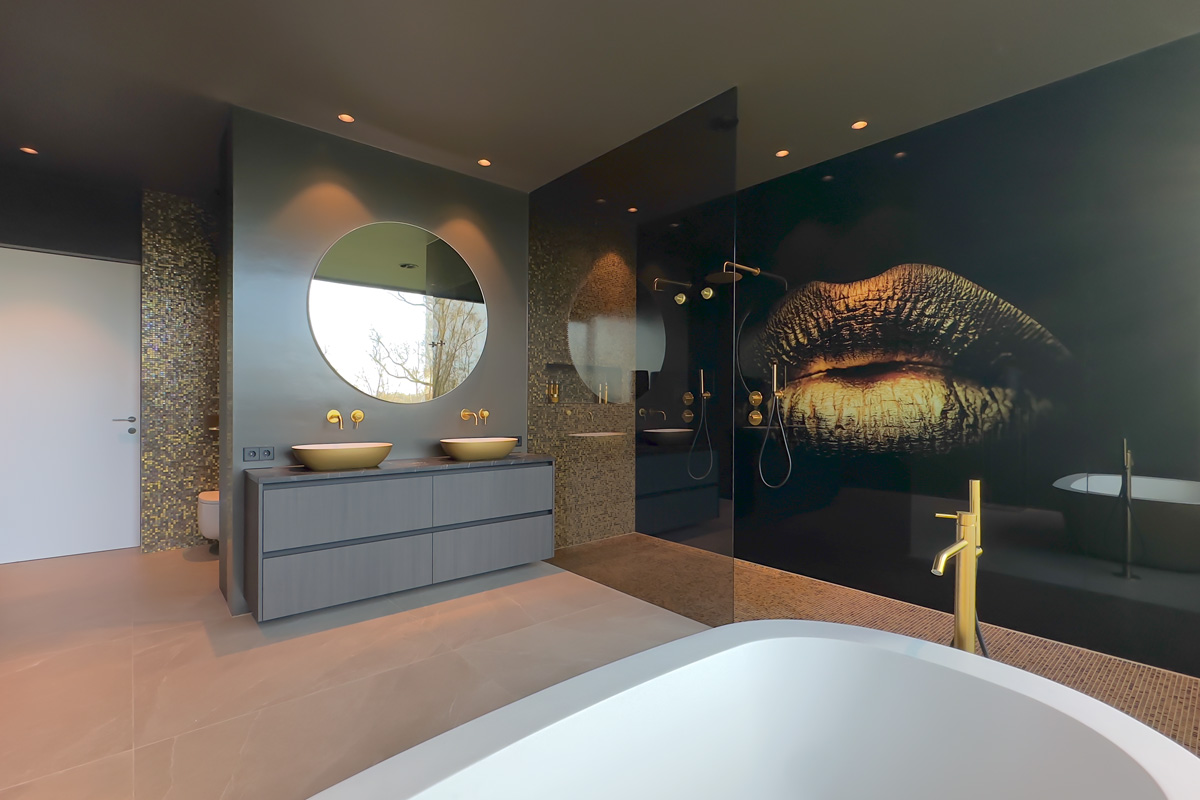 Luxe badkamer met gouden accenten, een vrijstaand bad, gouden kranen, een wastafelmeubel met ronde spiegel en een geprinte glasplaat met kunstzinnig lippenontwerp.