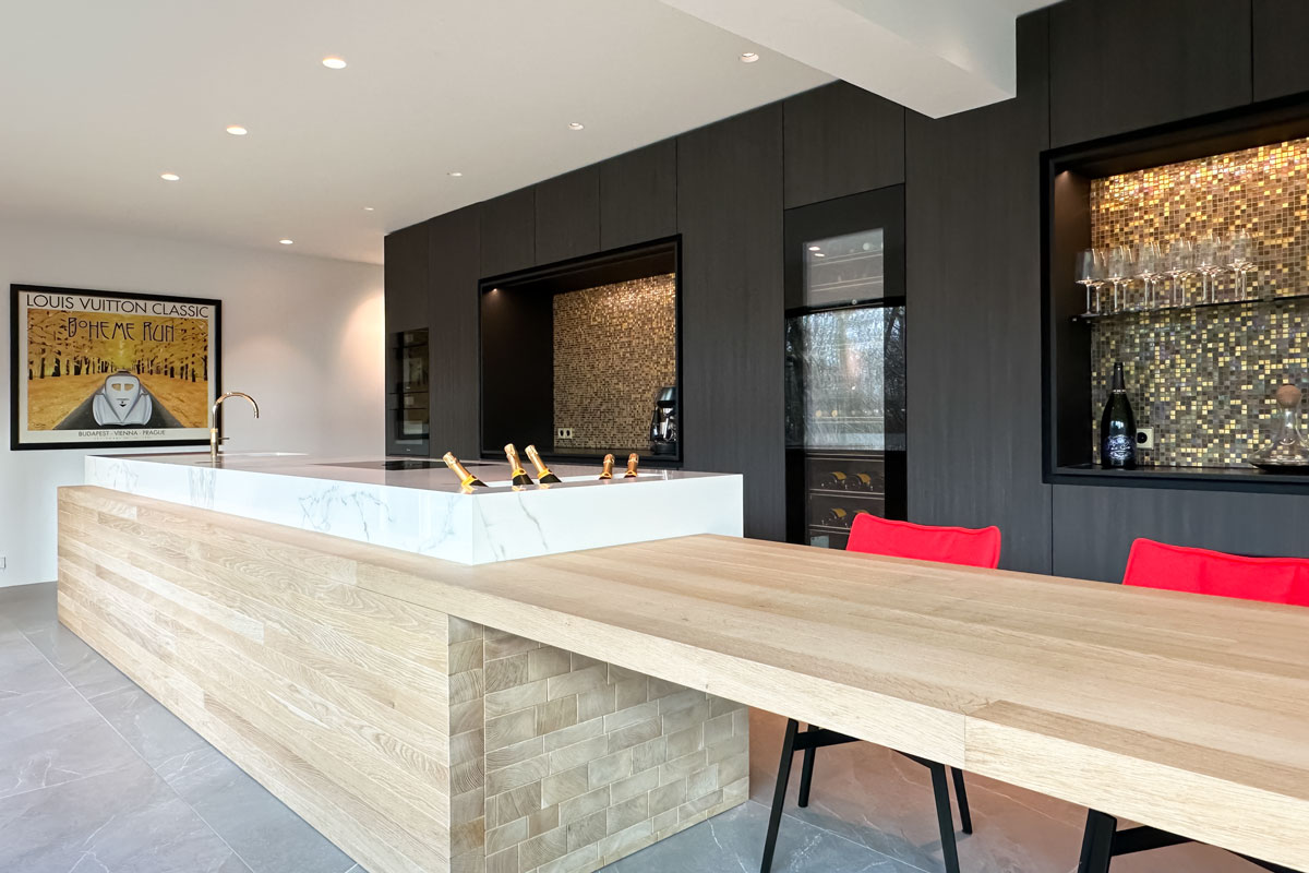 Luxe keuken met marmeren kookeiland, eikenhouten tafel, rode stoelen, en gouden details. Inclusief wandkasten met mozaïektegels en glazen wijnrekken.