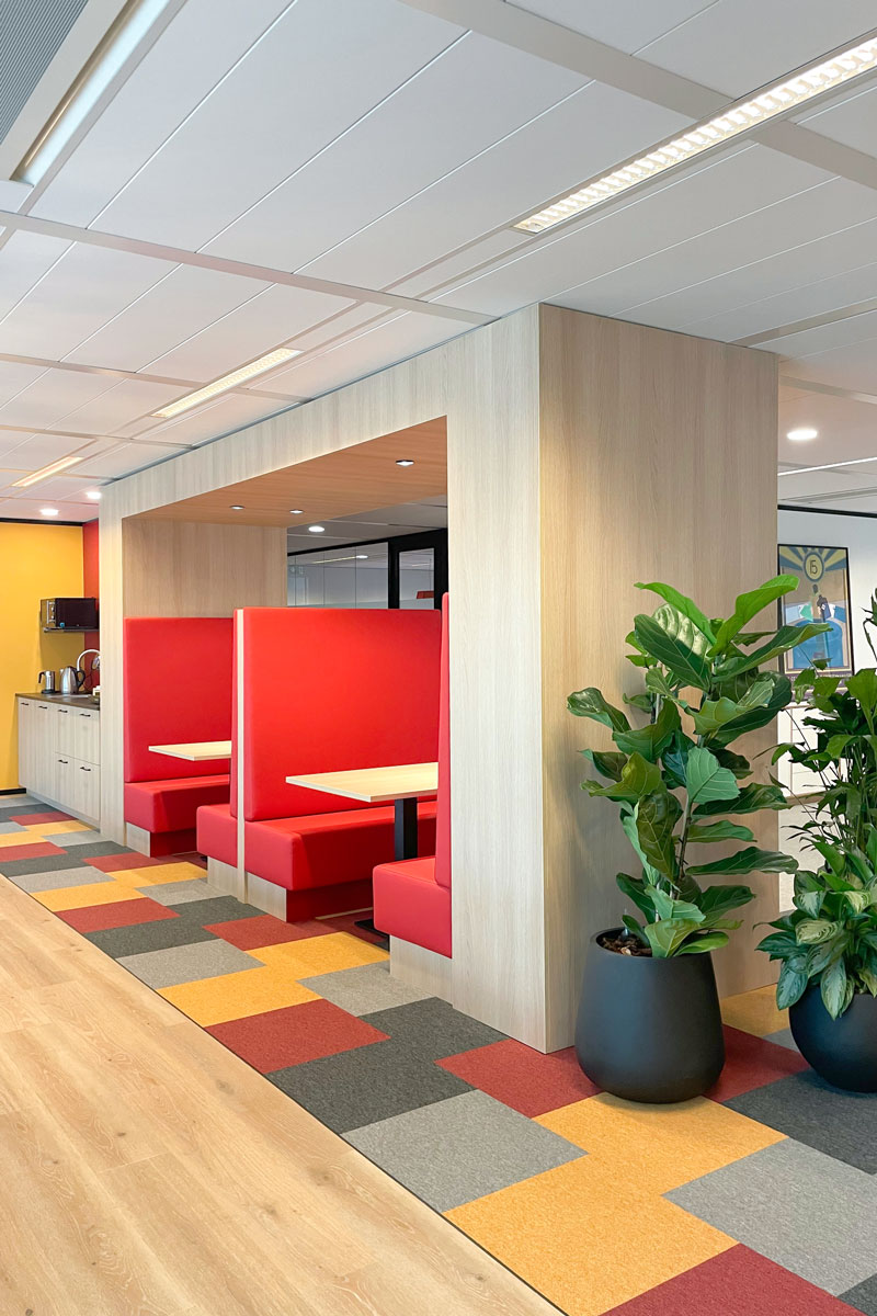 Kantoorinrichting Stoffenmanager, zithoek met rode bankjes, kleurrijke vloerbedekking en beplanting