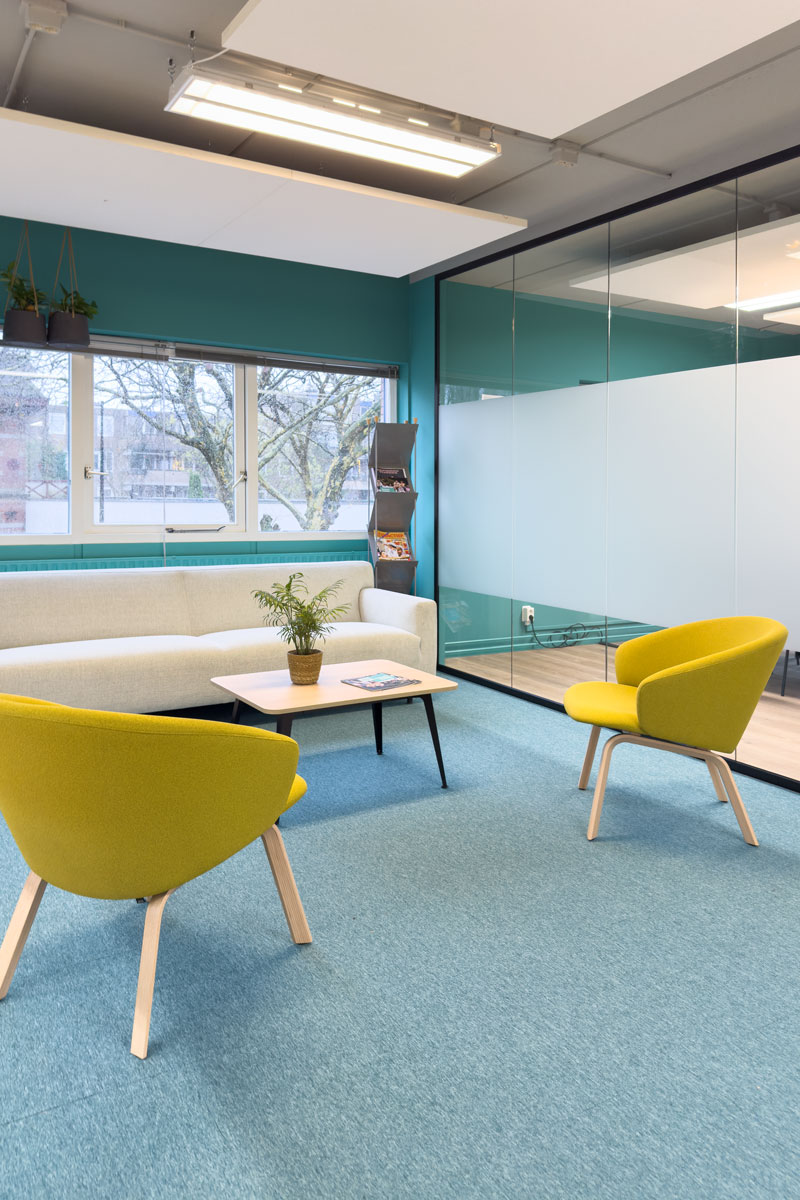 Kantoorinrichting Amsterdam: ontvangstruimte met gele fauteuils, glazen wanden en groene accentmuur bij Staij.