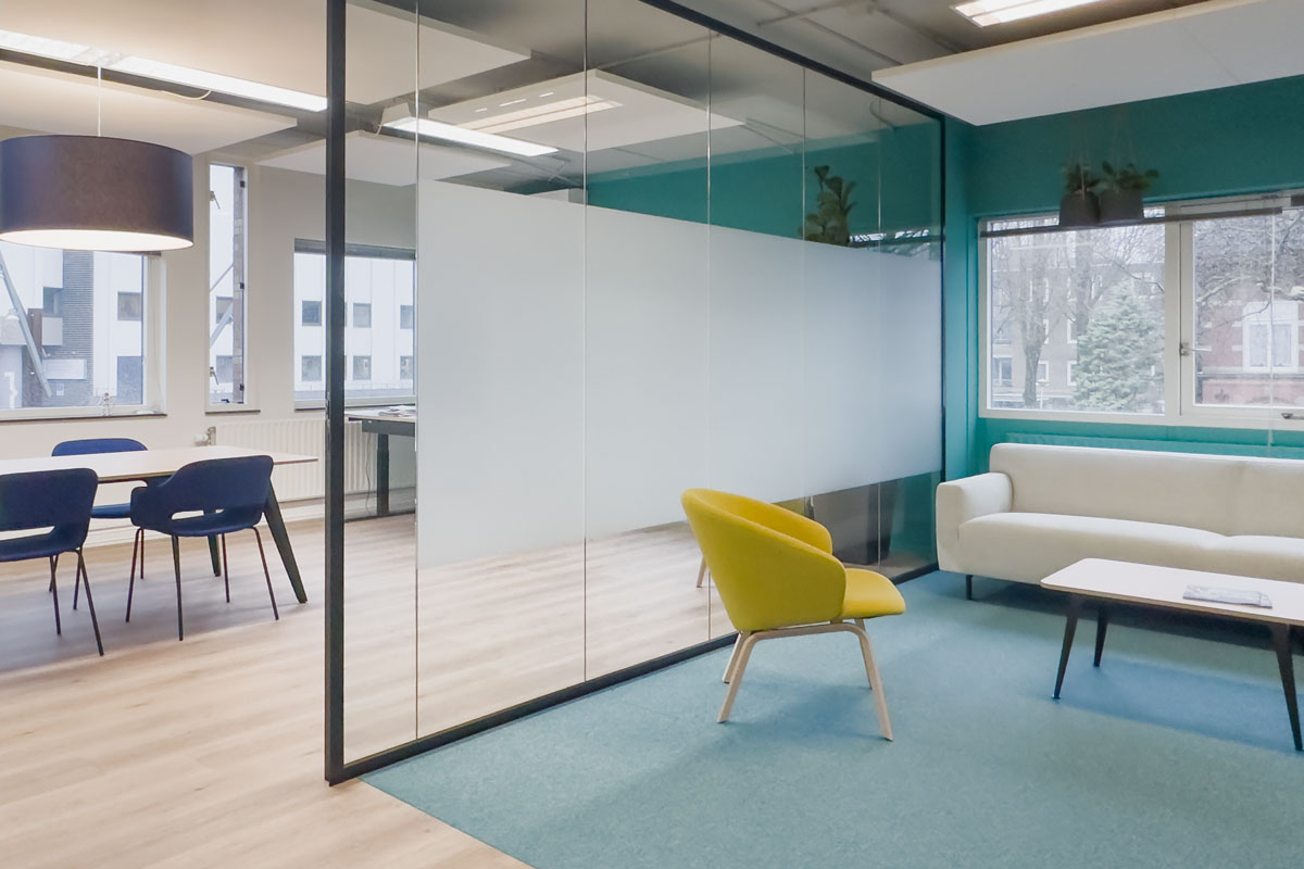 Moderne overlegplek in het kantoor van Staij Amsterdam met glazen wanden, groene accentmuur en een gele fauteuil.