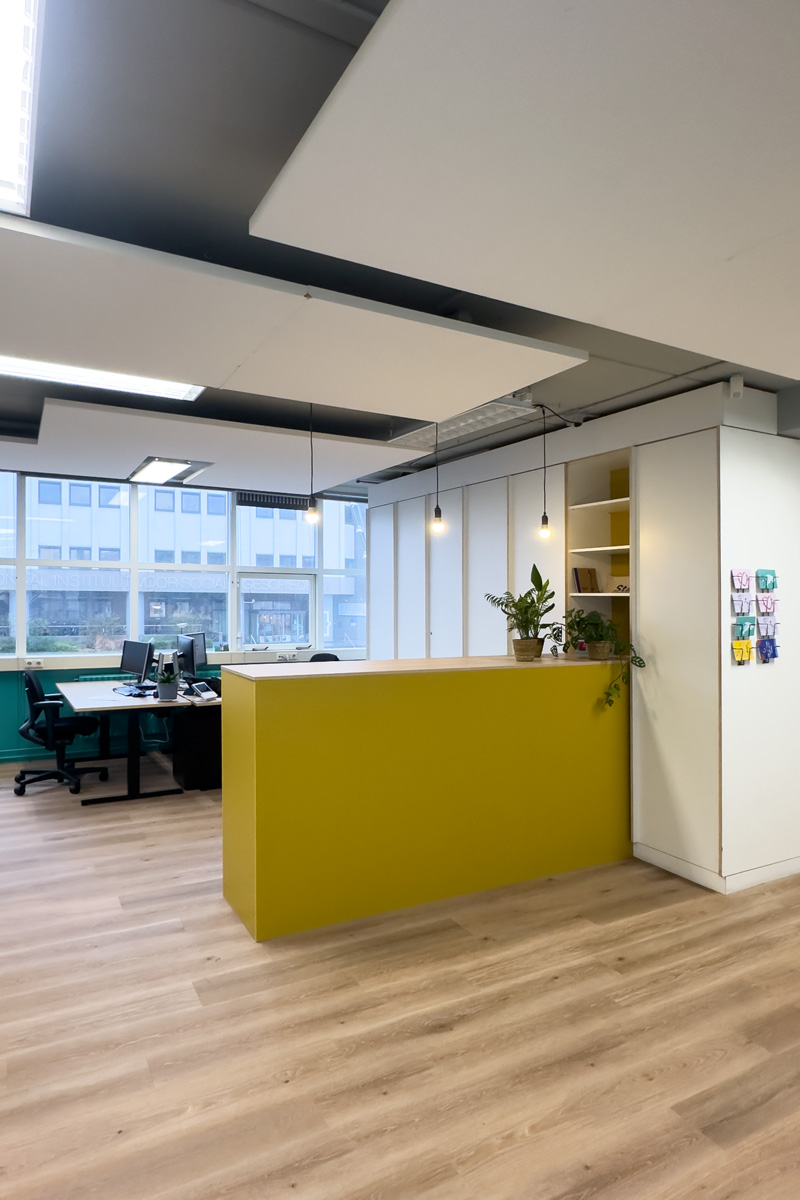 Kantoorinrichting Amsterdam: werkruimte met gele pantry, werkplekken en PVC vloer in warme houtprint bij Staij.