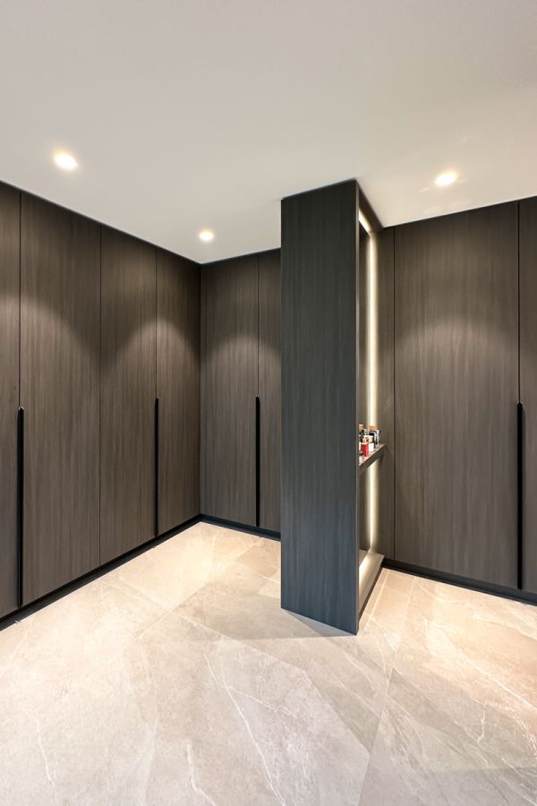 Luxe garderobekast met op maat gemaakte donkere houten panelen en geïntegreerde LED-verlichting. Ruime opbergruimte met een verfijnde afwerking en moderne uitstraling.