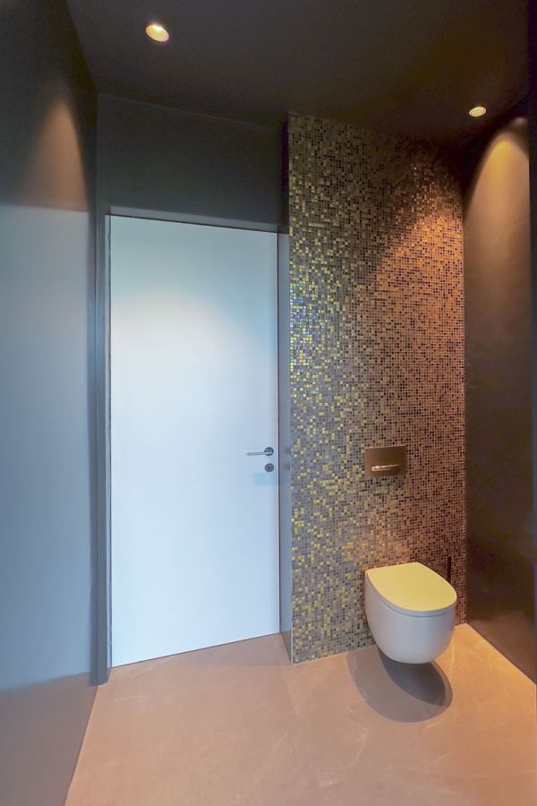 Luxe toilet met gouden mozaïektegels en een strak design. Minimalistisch afgewerkt met een modern hangend toilet en subtiele verlichting.