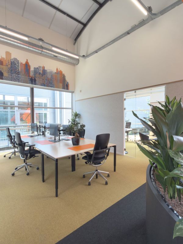 Kantoorruimte in het Condor-kantoor in Amersfoort met werkplekken, oranje accenten en skyline visual op de wand.