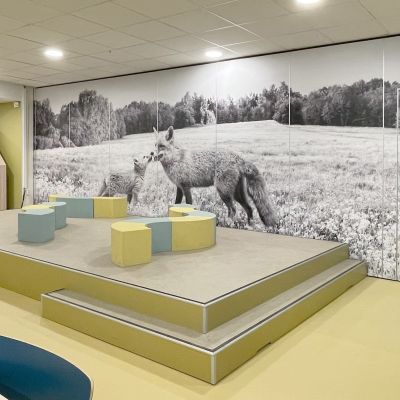  Leerplein in een basisschool met verhoogd podium en natuurthema-signing op de muur.