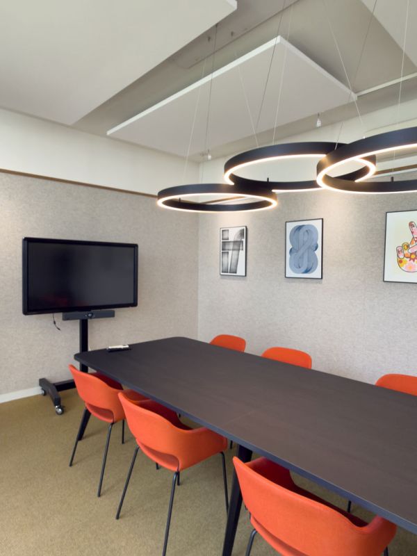 ergaderruimte met donkere tafel, oranje stoelen en ronde hangende armaturen