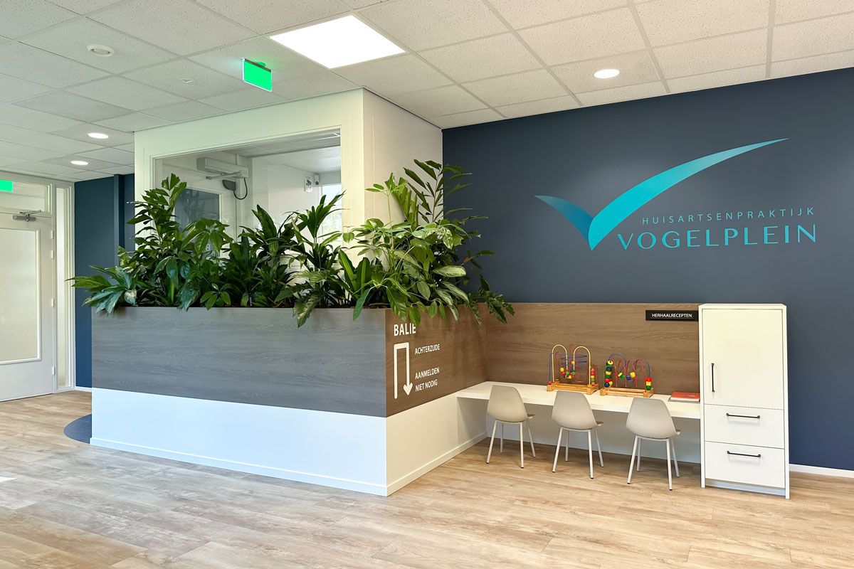 Wachtruimte met plantenbak en kinderhoek bij Huisartsenpraktijk Vogelplein. Houten look PVC vloer en modern interieur.