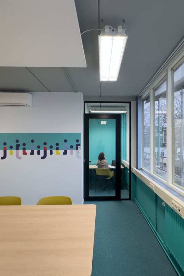 Stilteruimte in de moderne kantoorinrichting van Staij Amsterdam, met glazen wand, grafische prints en huisstijlkleuraccenten.