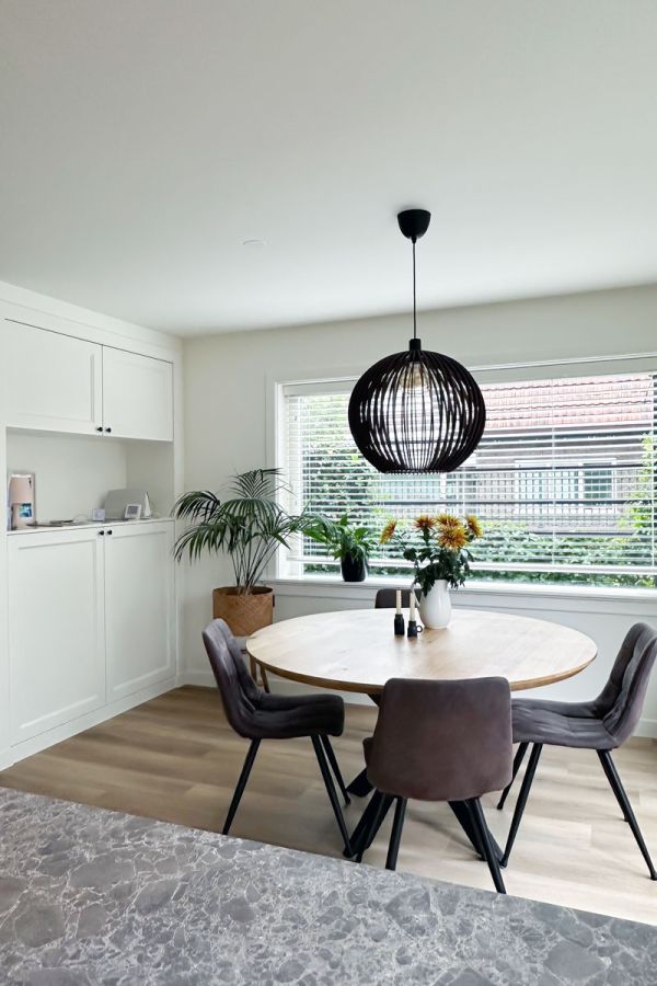 Lichte eetkamer in jaren 30 woning met ronde tafel, groene planten en grote raampartijen.