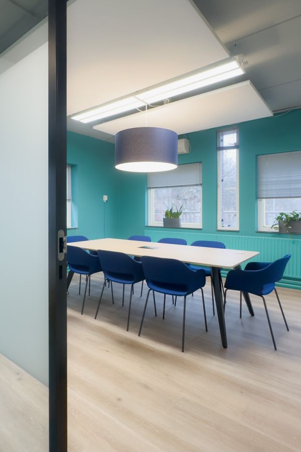 Kantoorinrichting Amsterdam: vergaderruimte met blauwe stoelen, houten vergadertafel en groene accentmuur bij Staij.