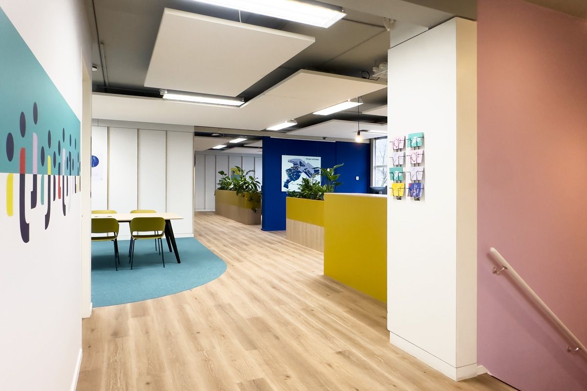 Overzicht van de kantoorinrichting met grafische prints in de huisstijl van Staij, moderne werkplekken en een centrale loopruimte met natuurlijke houten vloer.