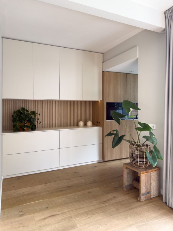 Wandkast en keuken op maat in beige kleur en houten latjes. met plant op de voorgrond.
