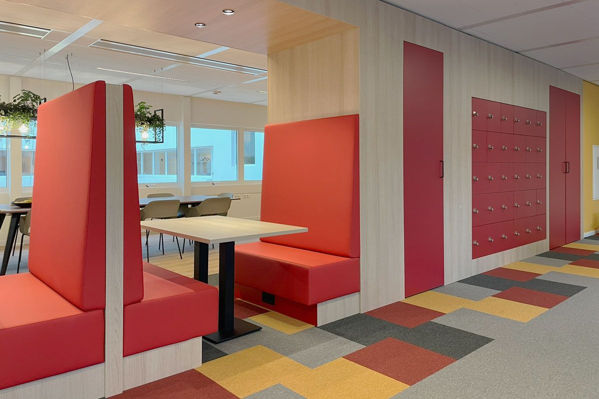 Op maat gemaakt meubel met rode treinbankjes, kluisjes en een vergadertafel op de achtergrond.