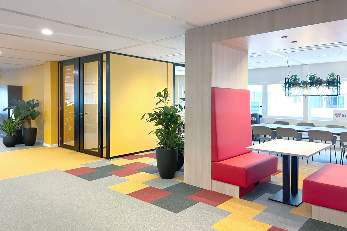 Flexibele kantoorinrichting met een vergaderruimte, rode treinbanken en groene planten als decoratie.