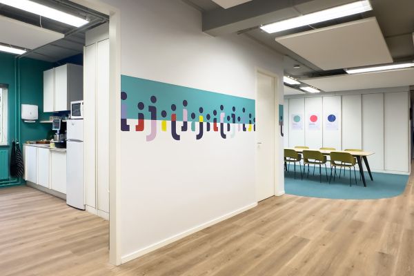 Kantoorinrichting Amsterdam: kleurrijke grafische wandprint, pantry en vergaderruimte bij Staij met PVC vloer in warme houtprint.