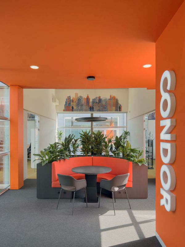 Entree Condor kantoor met oranje wand, verlicht logo en lounge met barkrukken