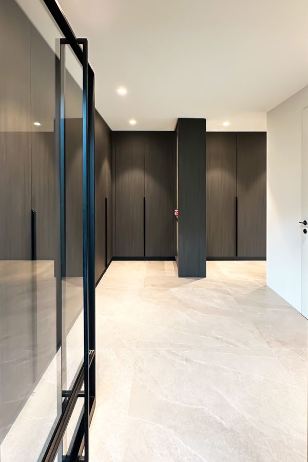 Luxe inloopkast met op maat gemaakte kasten in donkere houtkleur en strakke lijnen. Voorzien van geïntegreerde verlichting en moderne handgrepen.