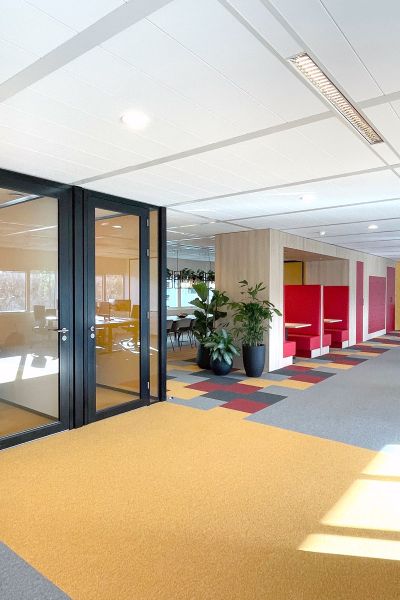 Kantoorinrichting Amstelveen: moderne werkruimte met glazen wanden, rode overlegplekken en kleurrijke tapijtzones.