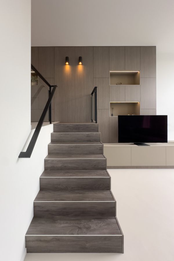 Maatwerkkast in een stijlvolle woonkamer met moderne trap en geïntegreerde tv-meubel.