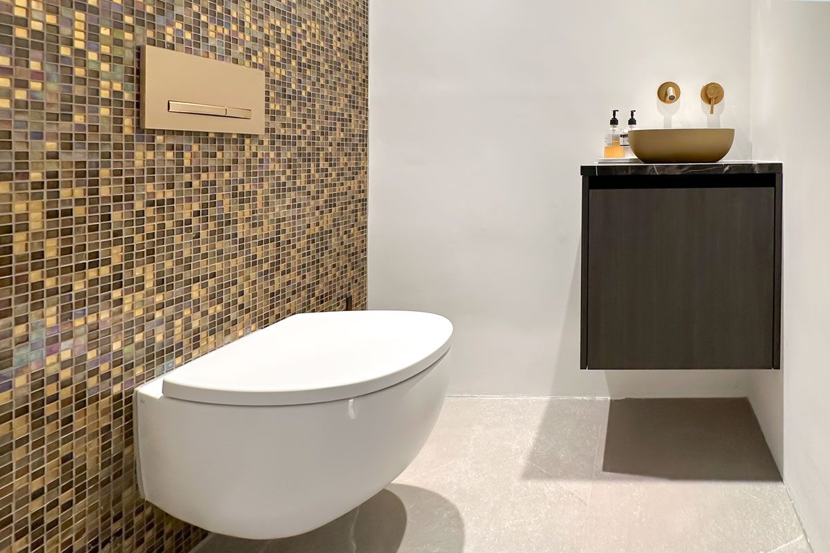 Luxe toilet met gouden mozaïektegels, een zwevend closet, een donker wastafelmeubel en gouden accenten.