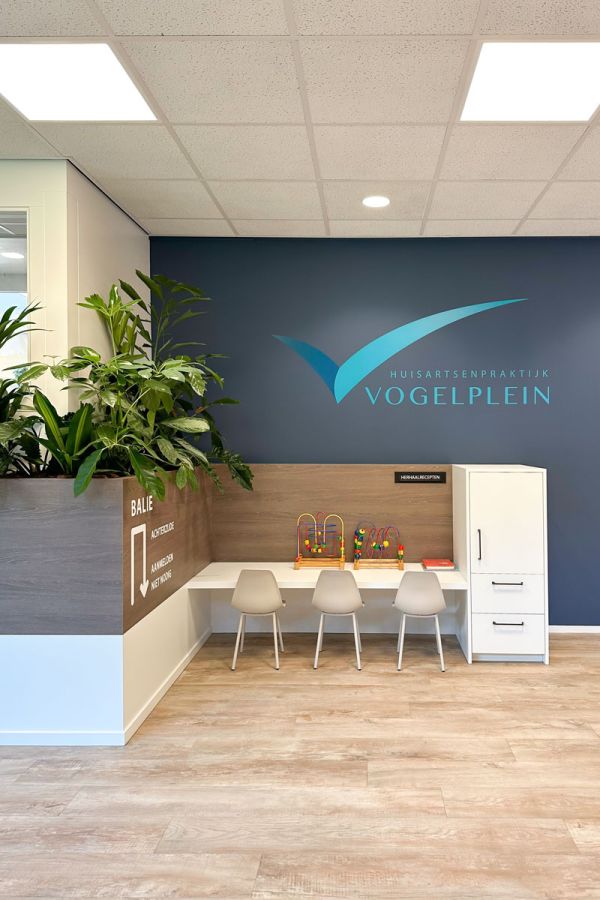 Wachtkamerinrichting met balie, plantenbak en houten look PVC vloer. Modern, licht ontwerp met veel groen en een leestafel.