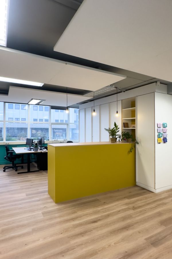 Kantoorinrichting Amsterdam: werkruimte met gele pantry, werkplekken en PVC vloer in warme houtprint bij Staij.