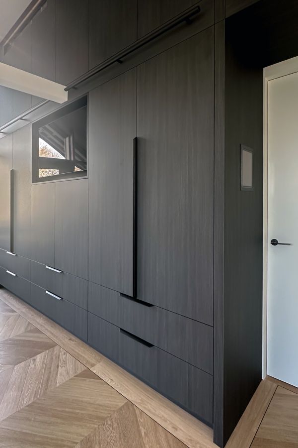 Luxe maatkast in een slaapkamer met donkere houten afwerking, voorzien van ingebouwde lades en strakke handgrepen, gecombineerd met een modern visgraatvloer.