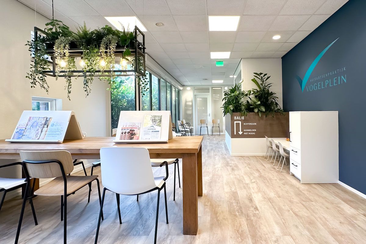 Wachtkamer inrichting met leestafel, plantenbakken en houten look PVC vloer. Fris en modern ontwerp bij Huisartsenpraktijk Vogelplein.