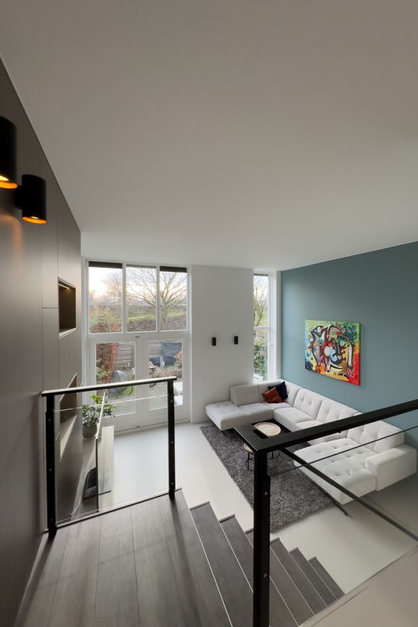 Moderne woonkamer in een interieur op maat met grote ramen, een stijlvolle bank, kleurrijke kunst en een balustrade op maat in Amersfoort.
