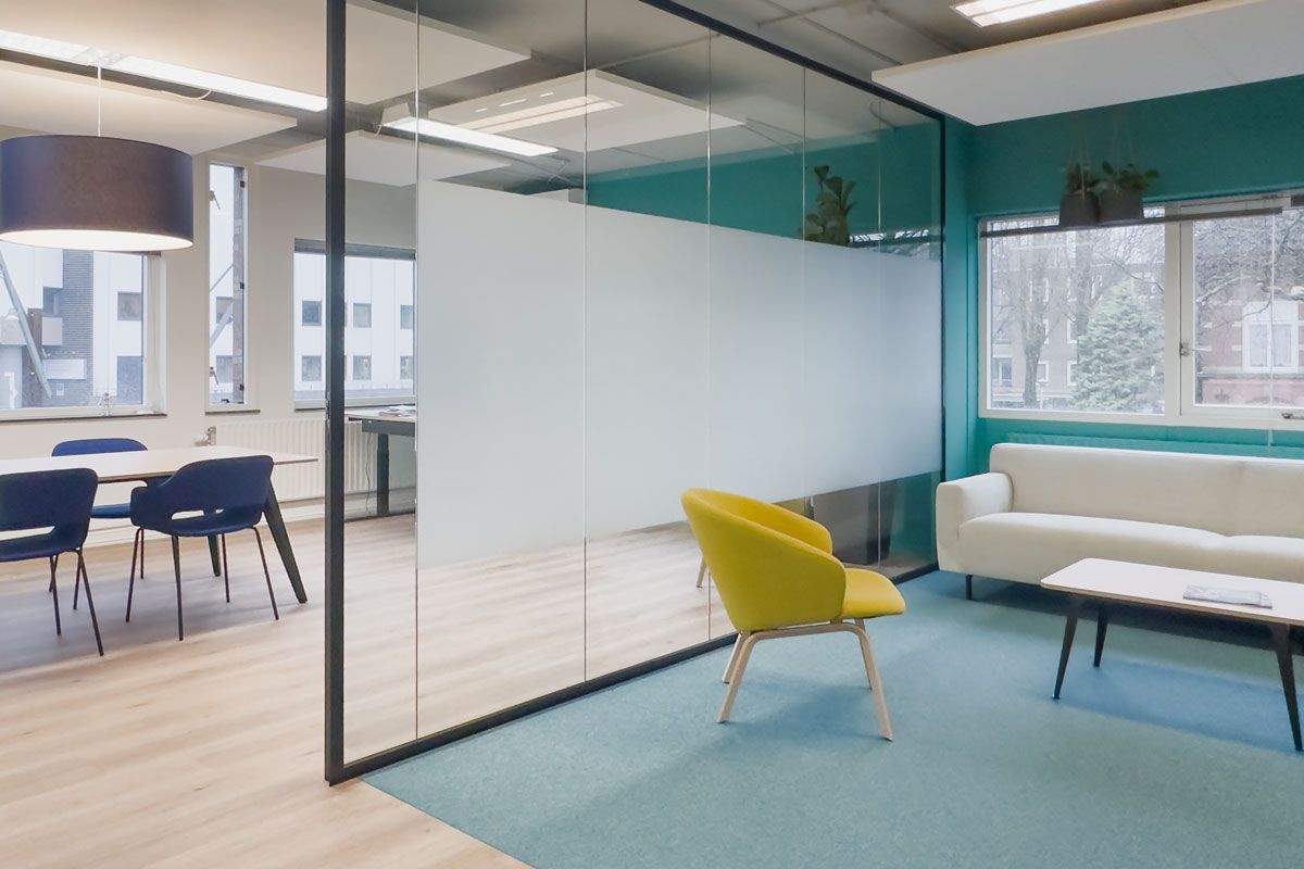 Moderne overlegplek in het kantoor van Staij Amsterdam met glazen wanden, groene accentmuur en een gele fauteuil.