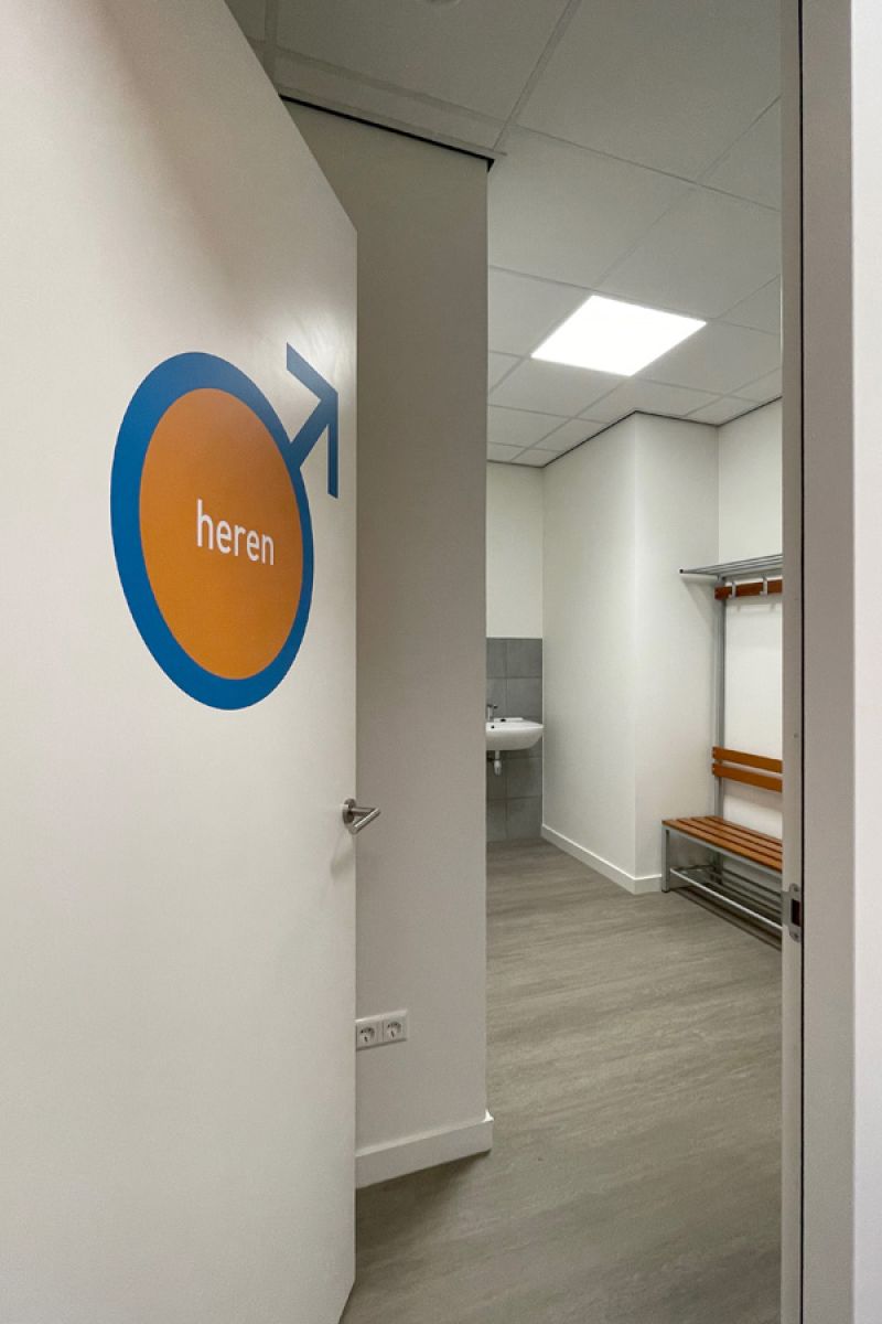 Kleedkamer in een fysiopraktijk met opvallende signing en praktische inrichting.