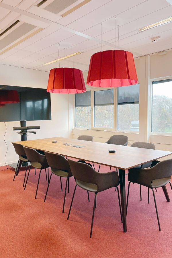 Vergaderruimte in het kantoor van Stoffenmanager in Amstelveen, met rode lampen, een houten tafel en comfortabele stoelen.