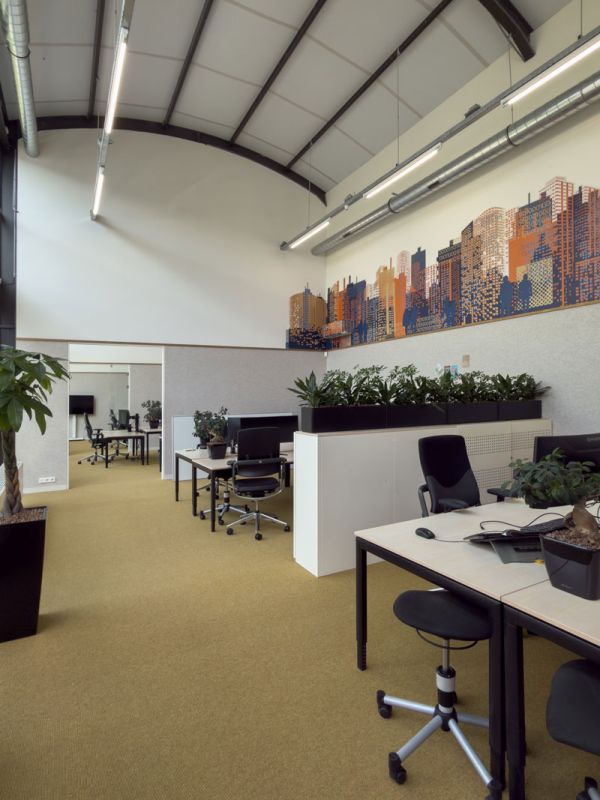 Open werkruimte met bureaus, ergonomische stoelen en groene plantenbakken