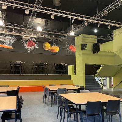 Aula van een school met moderne inrichting, industriële accenten en kleurrijke signing.